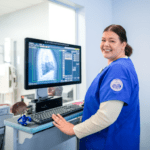 A female radiologic technology student smiling next to an x-ray